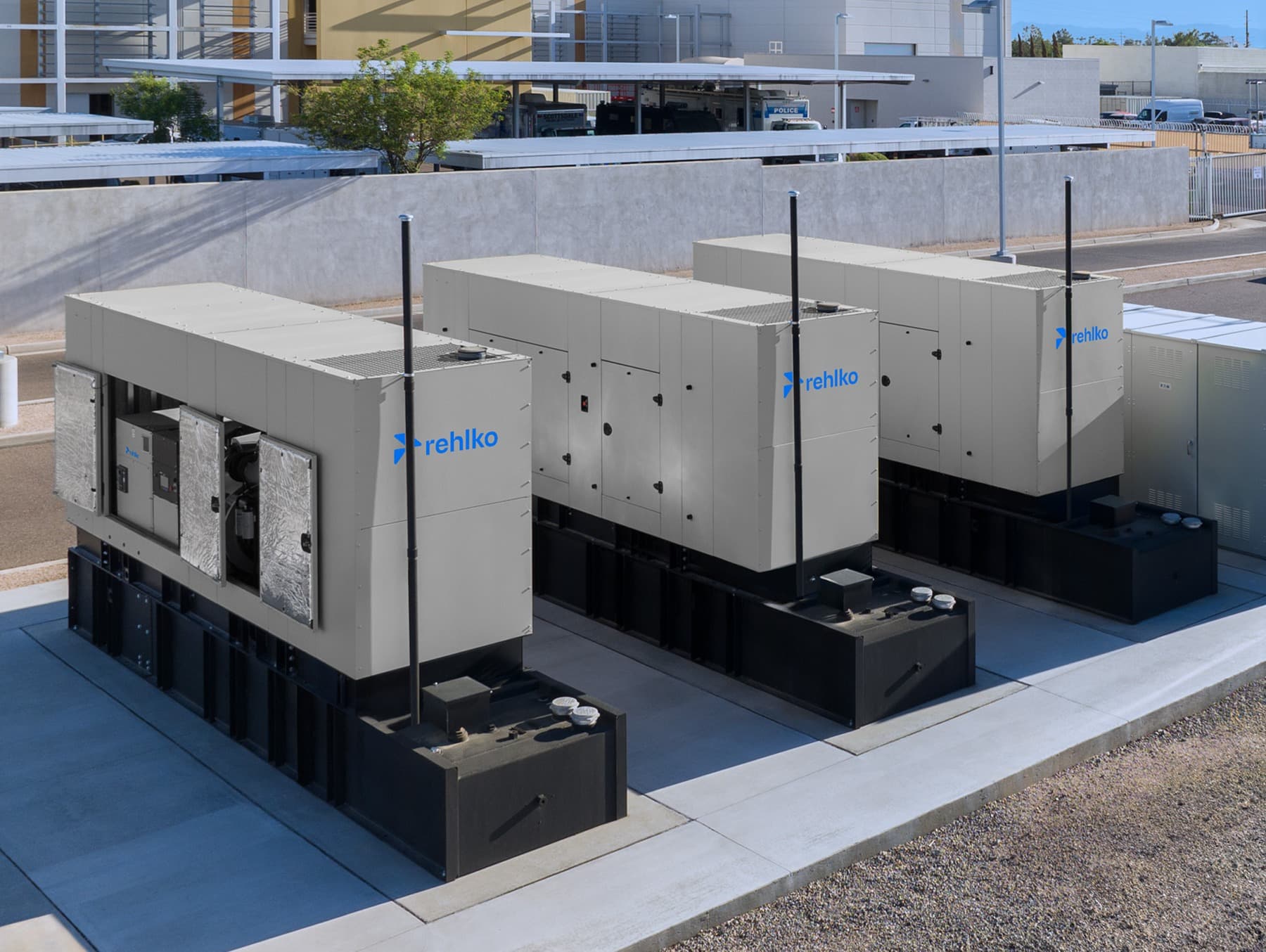 Three Rehlko enclosure generators side by side beside a building.